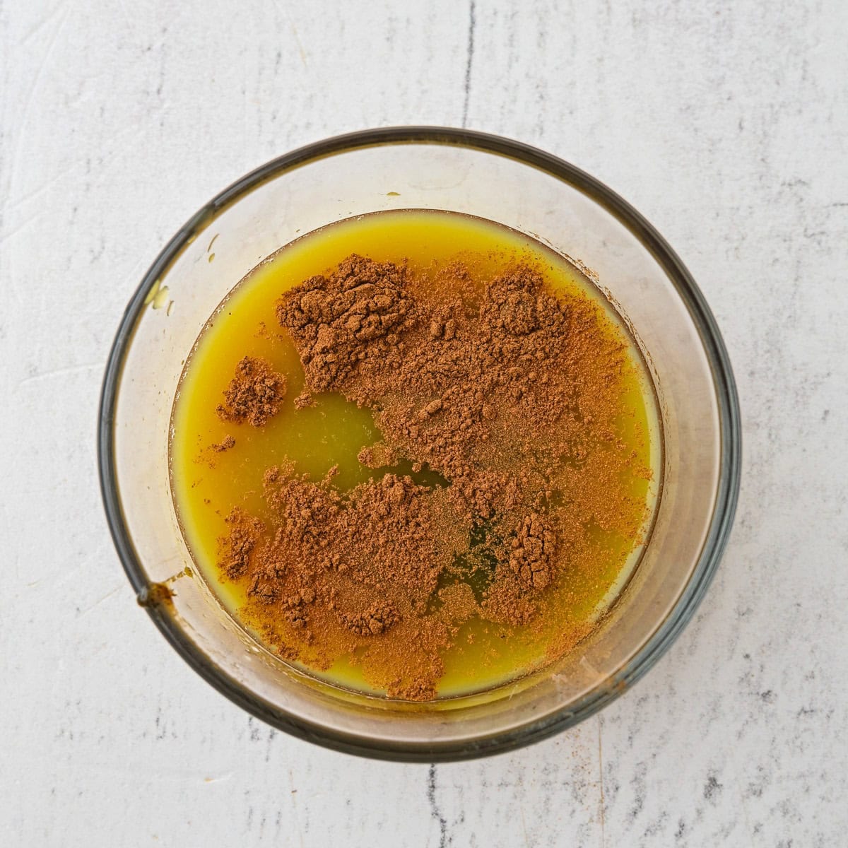 A glass bowl containing melted butter and cocoa powder on a white surface—perfect for whipping up a solo dessert after your Thanksgiving dinner for one.