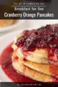 A stack of pancakes for one topped with cranberry orange sauce, served on a white plate. Text reads: Breakfast for One: Cranberry Orange Pancakes.