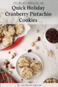 A plate of cranberry pistachio cookies is surrounded by scattered dried cranberries and pistachios, with more cookies on parchment paper nearby. Text reads Quick Holiday Cranberry Pistachio Cookies.