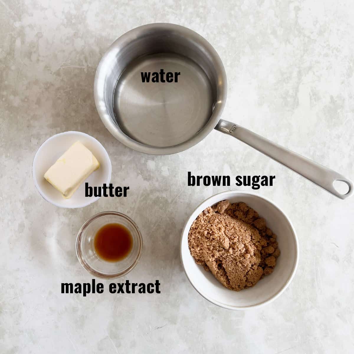 A saucepan with water, a bowl of butter, a bowl of brown sugar, and a small dish of maple extract are arranged on a light countertop.