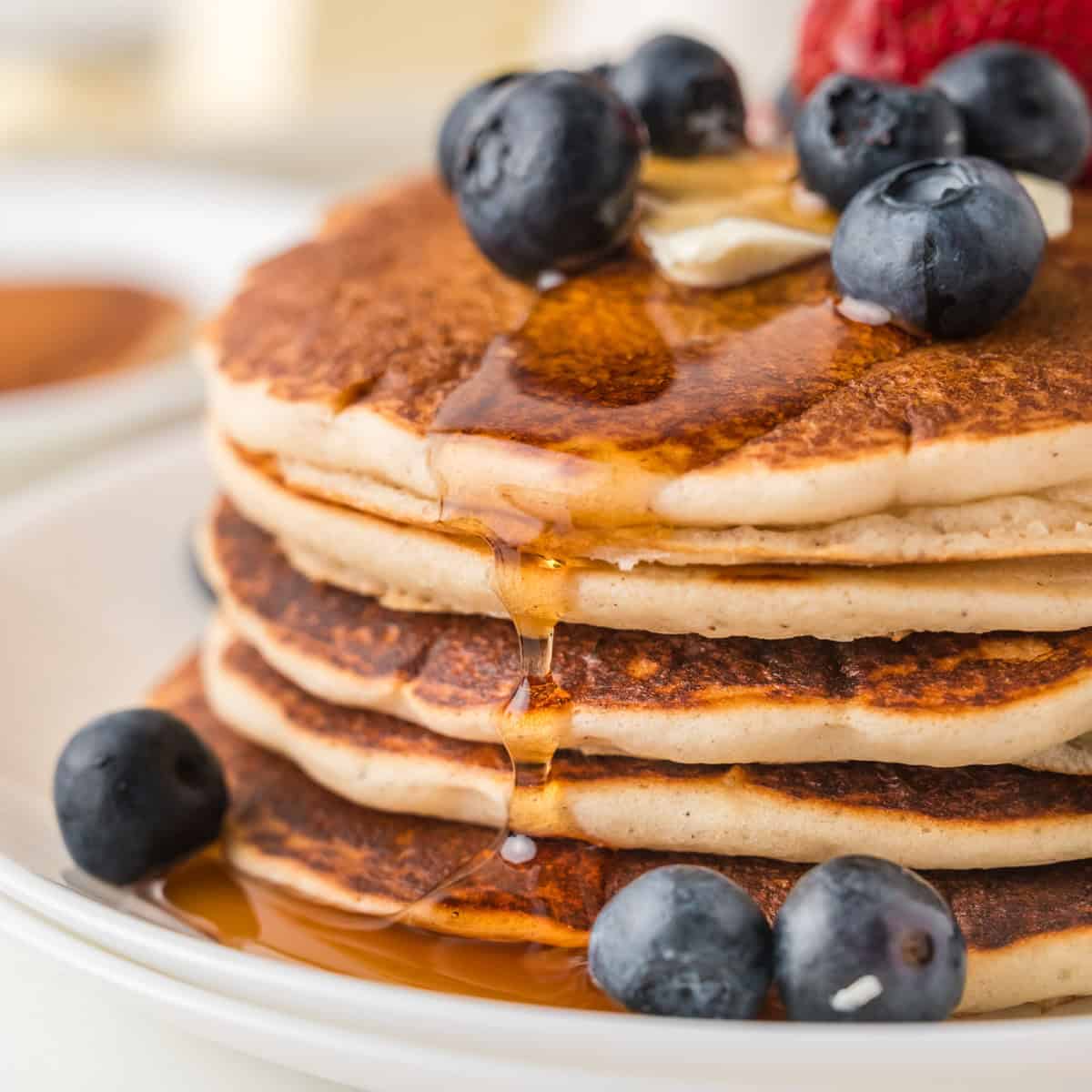 A stack of pancakes topped with blueberries, a pat of butter, and syrup on a white plate.