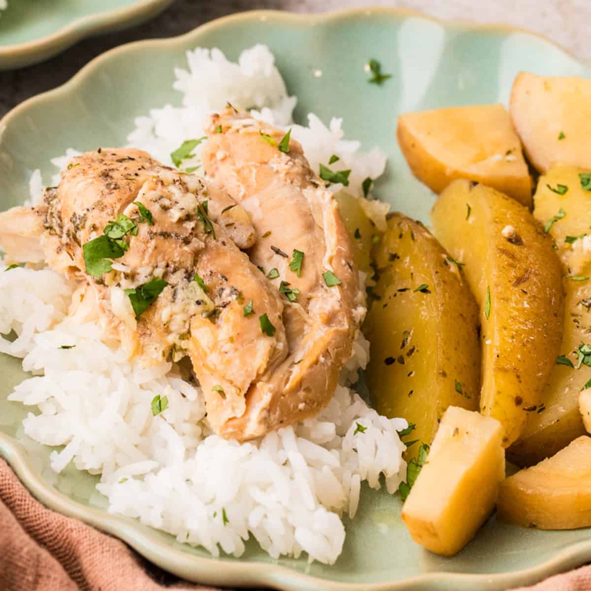 A plate with white rice topped with cooked chicken, garnished with herbs, served alongside roasted potato wedges.
