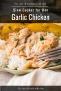 A plate of shredded garlic chicken served over white rice with a fork, garnished with herbs and paired with sliced potatoes. Text overlay reads Slow Cooker for One Garlic Chicken.