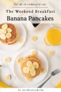 Overhead view of two plates of banana pancakes topped with banana slices, a glass of orange juice, syrup, and scattered banana slices on a white table.