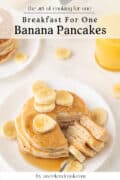A plate of banana pancakes topped with banana slices, surrounded by more banana pieces, with a glass of orange juice in the background.
