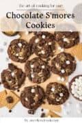 A batch of chocolate smores cookies with marshmallows, chocolate chunks, and graham crackers on a parchment-lined surface.