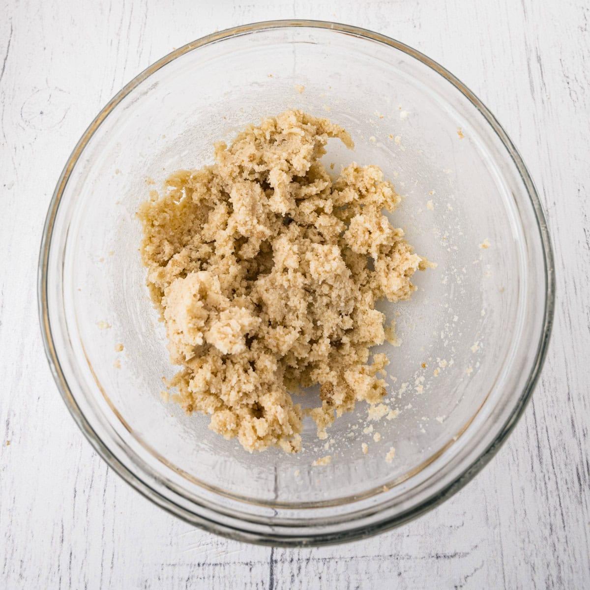 A clear glass bowl containing a mixture of creamed butter and sugar sits on a white wooden surface.