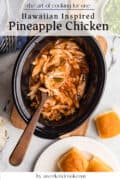 Slow-cooked pineapple chicken in a black crockpot with a wooden spoon, served with two bread rolls on a white plate and sliced green onions nearby.