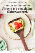 A slice of ricotta and spinach egg white casserole with cherry tomatoes on a plate, next to a wooden spatula and a striped towel. Text overlay promotes a make-ahead breakfast recipe.