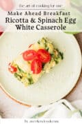 A slice of ricotta and spinach egg casserole topped with cherry tomato halves sits on a light green plate.