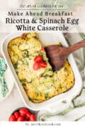 A baked ricotta and spinach egg white casserole in a white dish, with a wooden spatula serving a portion, garnished with sliced cherry tomatoes.