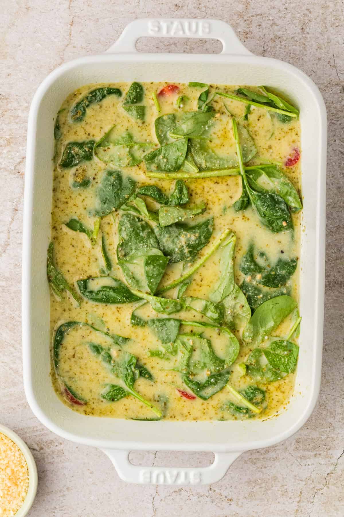 White ceramic baking dish filled with a fresh spinach and seasoning mixture, perfect for creating a wholesome egg white casserole on a light countertop.