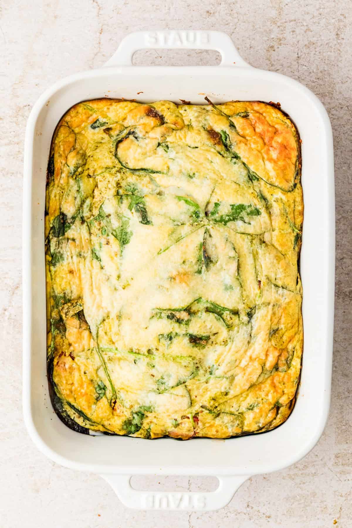 A baked spinach and cheese egg white casserole in a white rectangular ceramic dish on a light-colored surface.