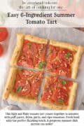 A rectangular tomato tart, cut into four pieces, topped with sliced tomatoes and basil, sits on parchment paper with fresh tomatoes nearby.
