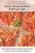 A sliced tomato and garlic puff pastry tart with visible tomato slices, herbs, and a garnish of basil on parchment paper.