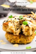 Two tuna patties topped with spicy mayo, black sesame seeds, and green onions, served on a plate. Text on image reads Dinner for One: Tuna Patties with Spicy Mayo.
