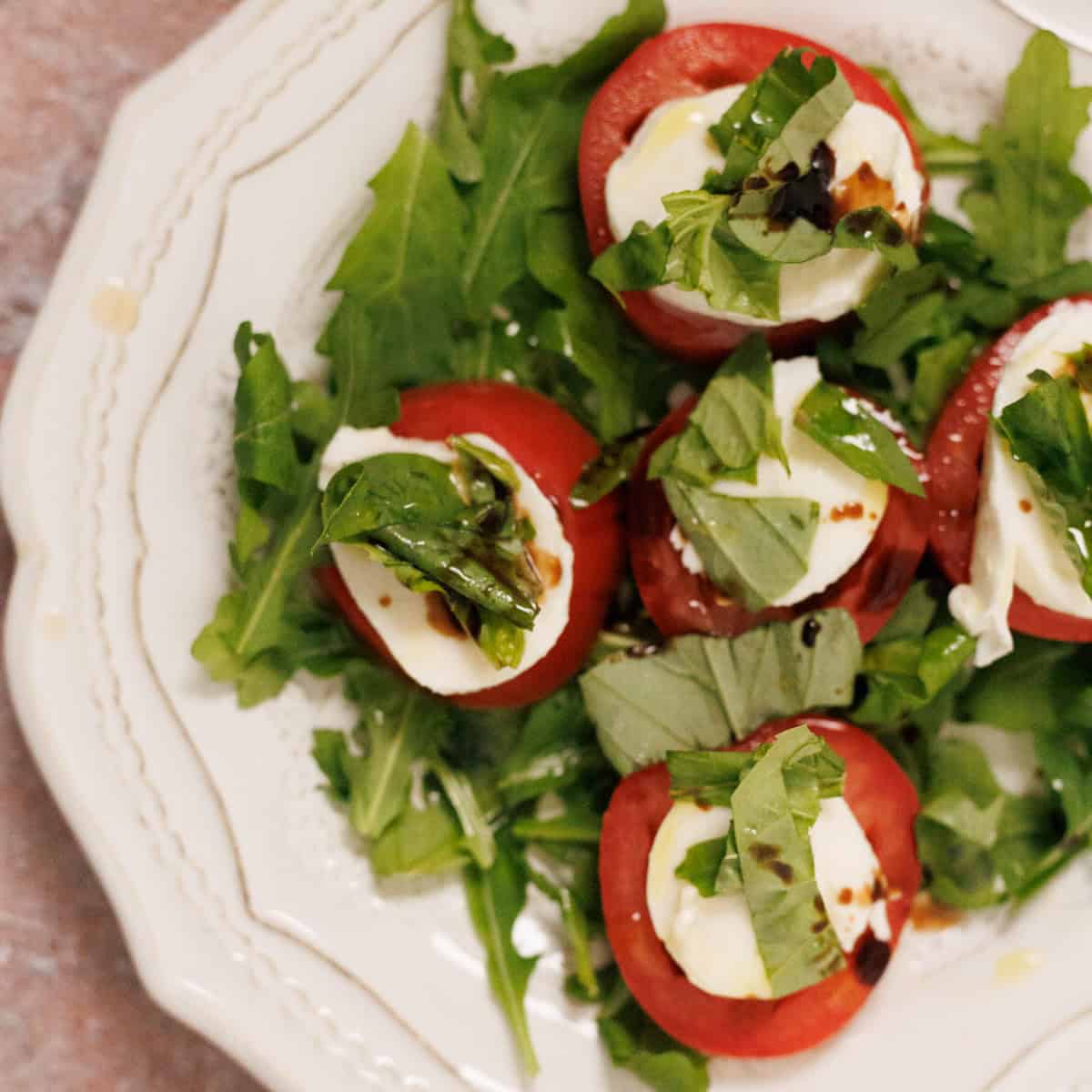 A plate of sliced tomatoes and mozzarella with fresh basil and balsamic glaze, served on a bed of arugula.