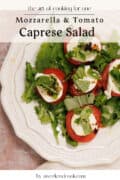 Plate of Caprese salad with sliced tomatoes, mozzarella, fresh basil, arugula, and a drizzle of balsamic glaze on a white dish.
