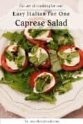 A plate of caprese salad with sliced tomatoes, mozzarella, fresh basil, and arugula, drizzled with balsamic dressing, on a white decorative plate.
