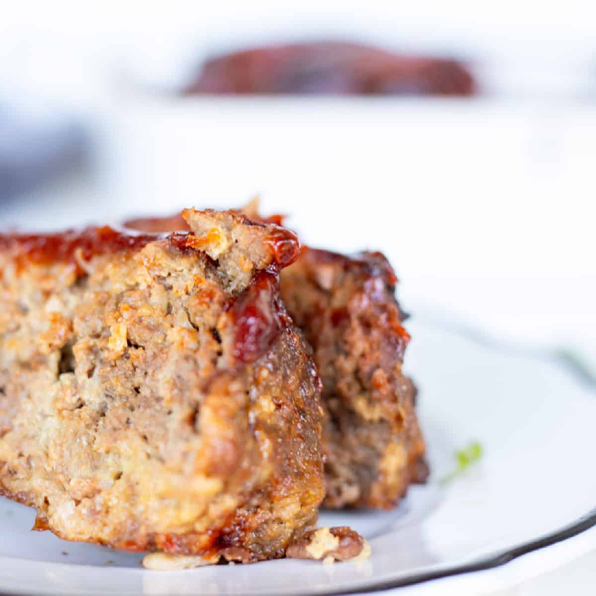 Close-up of two slices of glazed meatloaf on a white plate with a blurred background—showcasing how to keep meatloaf moist and avoid common meatloaf mistakes.