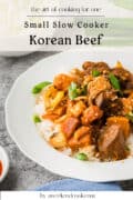 A plate of slow cooker Korean beef stew with vegetables and rice, garnished with green onions and sesame seeds, sits on a white dish. Text on the image promotes a simple recipe for one.
