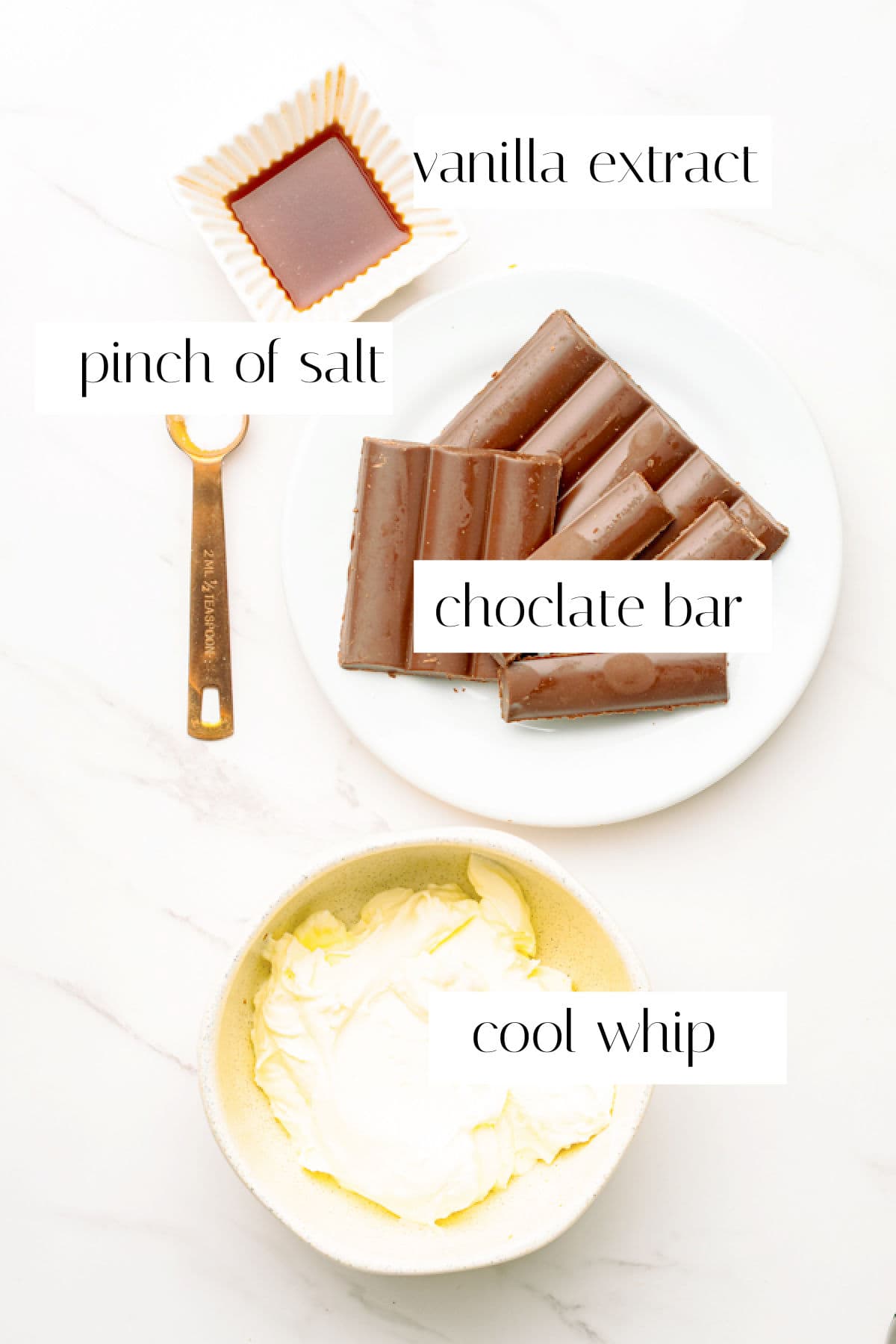 A bowl of Cool Whip, a plate with chocolate bars, a small dish of vanilla extract, and a measuring spoon with salt are arranged on a white surface.
