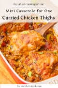 A baking dish with two cooked curried chicken thighs in a rich sauce, garnished with herbs, and a wooden spoon lifting one piece. Text reads Curried Chicken Thighs - Mini Casserole for One.