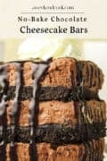 Close-up of stacked no-bake chocolate cheesecake bars with chocolate drizzle and a dollop of whipped cream on top.