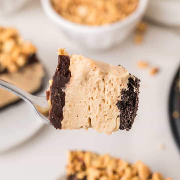 A close-up of a fork holding a bite of layered dessert with a creamy filling, chocolate base, and cookie crust.