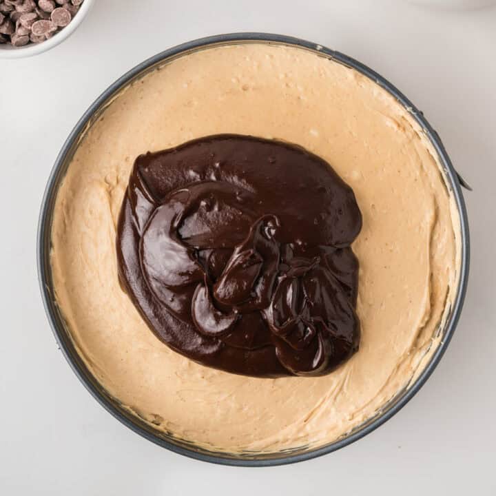 A springform pan filled with peanut butter cheesecake batter topped with a layer of chocolate ganache, viewed from above.