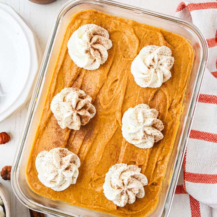 A rectangular glass dish filled with creamy pumpkin dessert, topped with six swirls of whipped cream and a dusting of cinnamon.