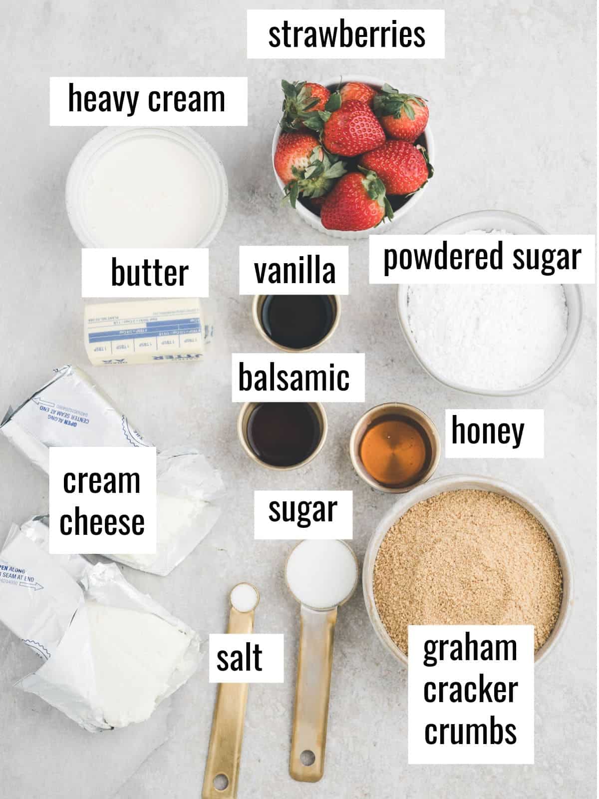 Top-down view of labeled ingredients for a dessert, including heavy cream, strawberries, butter, vanilla, powdered sugar, cream cheese, balsamic, honey, sugar, salt, and graham cracker crumbs.