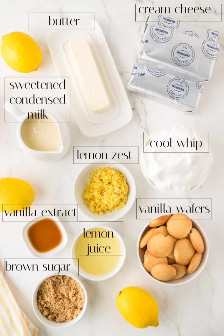 Ingredients including butter, cream cheese, sweetened condensed milk, lemon zest, cool whip, vanilla extract, vanilla wafers, brown sugar, lemon juice, and whole lemons on a white surface.