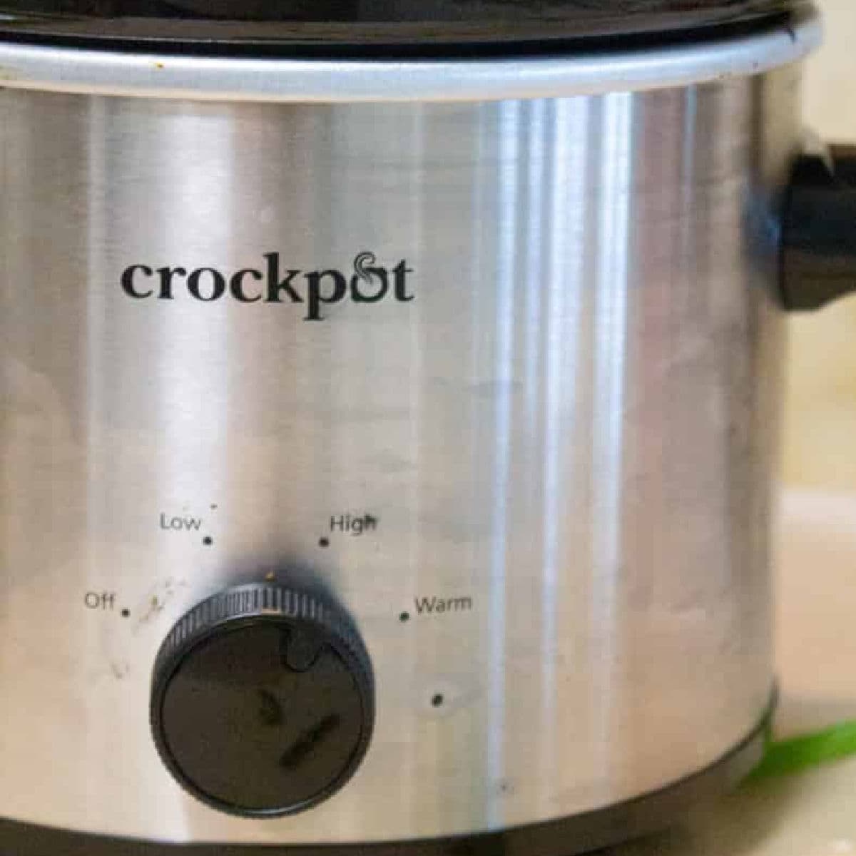 A stainless steel crockpot with a black dial showing Off, Low, High, and Warm settings—perfect for trying a new small-batch slow cooker recipe. The lid and handle are partially visible.
