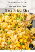 A close-up shot of easy fried rice with peas, carrots, and scrambled eggs on a wooden spoon over a pan of fried rice.