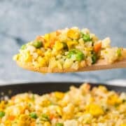 A wooden spoon scoops a serving of fried rice with peas, carrots, and scrambled egg.