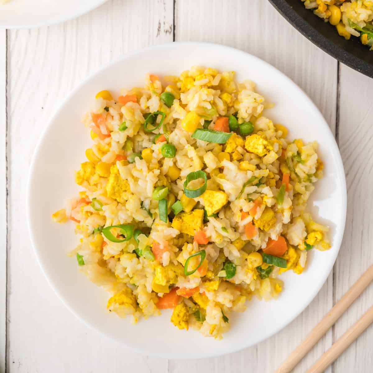 Fried rice with egg, peas, carrots, and corn on a white plate, with chopsticks.