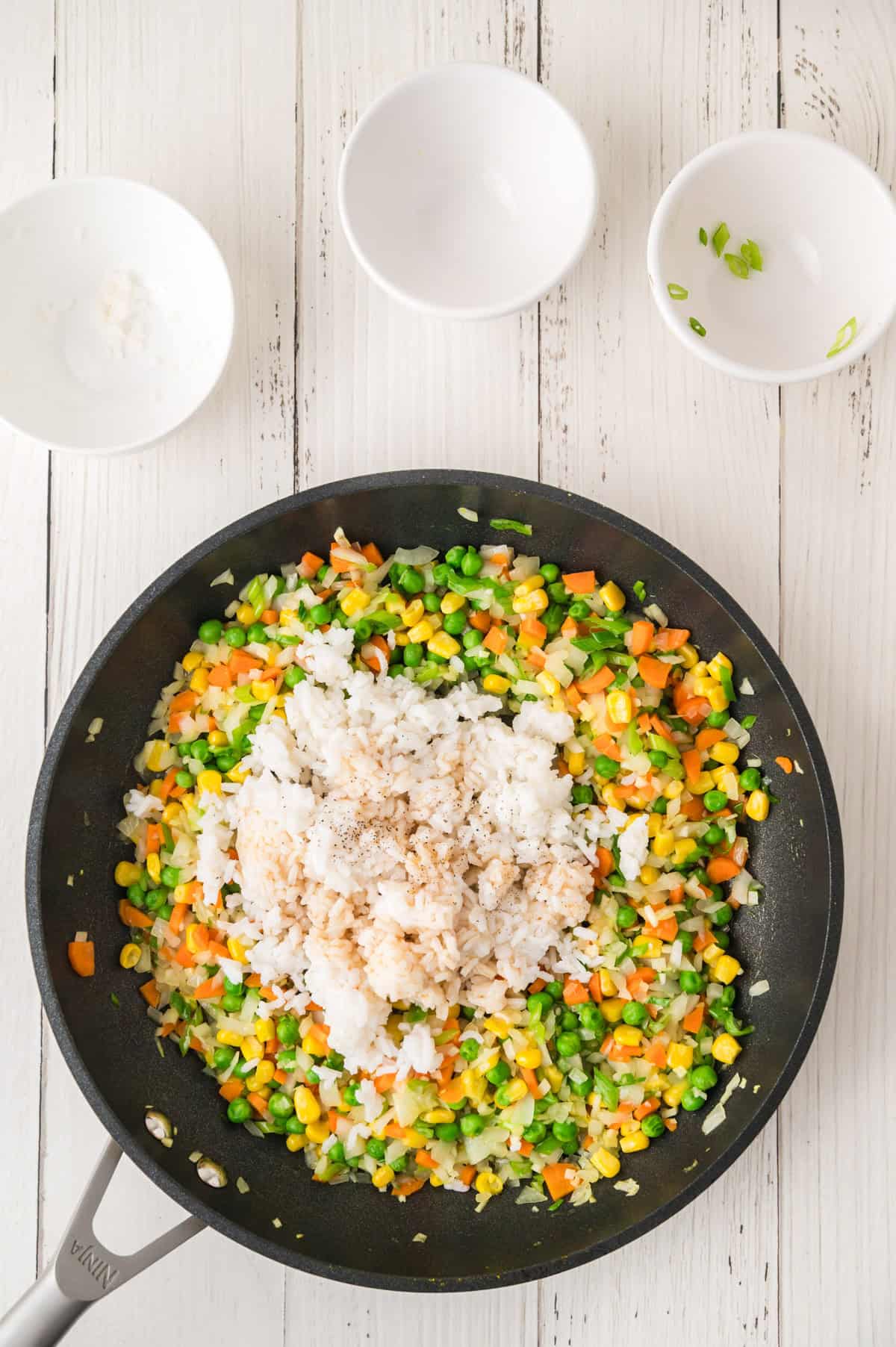 Fried rice with peas, carrots, corn, and onions being prepared in a black frying pan.