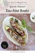 Two zucchini boats filled with a savory meat mixture and topped with grated cheese, served on a white plate with a garnish, photographed from above.