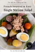 A bowl of classic Nicoise salad with tuna, green beans, potatoes, hard-boiled eggs, olives, and cherry tomatoes is beautifully arranged and viewed from above.