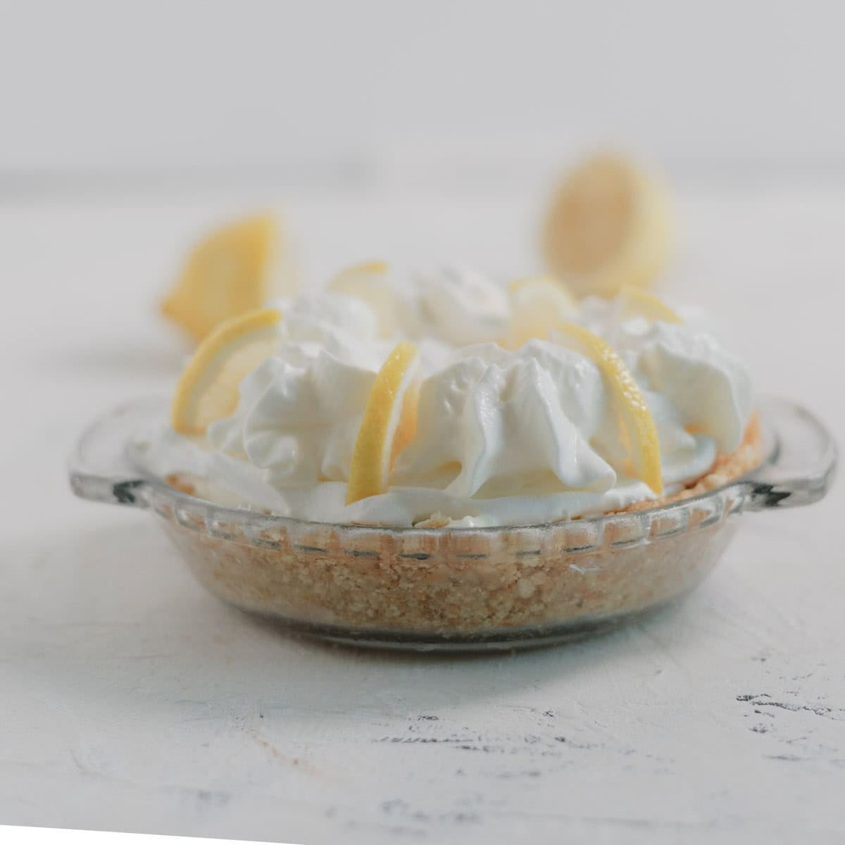 A mini lemon cheesecake in a glass dish topped with whipped cream and lemon slices.