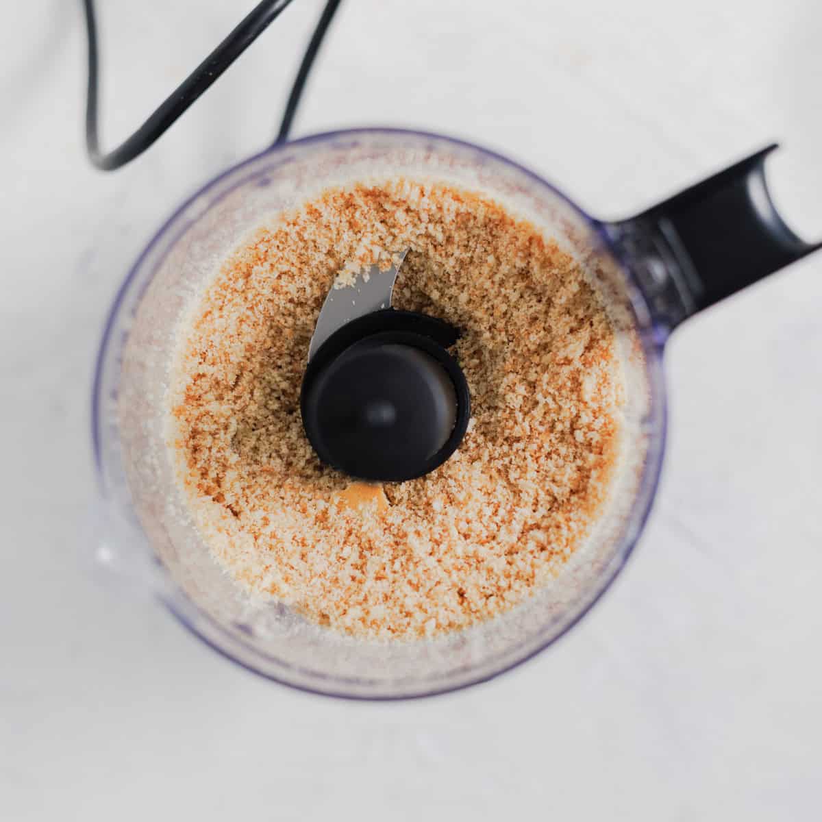Food processor containing freshly processed breadcrumbs for a no-bake cheesecake.
