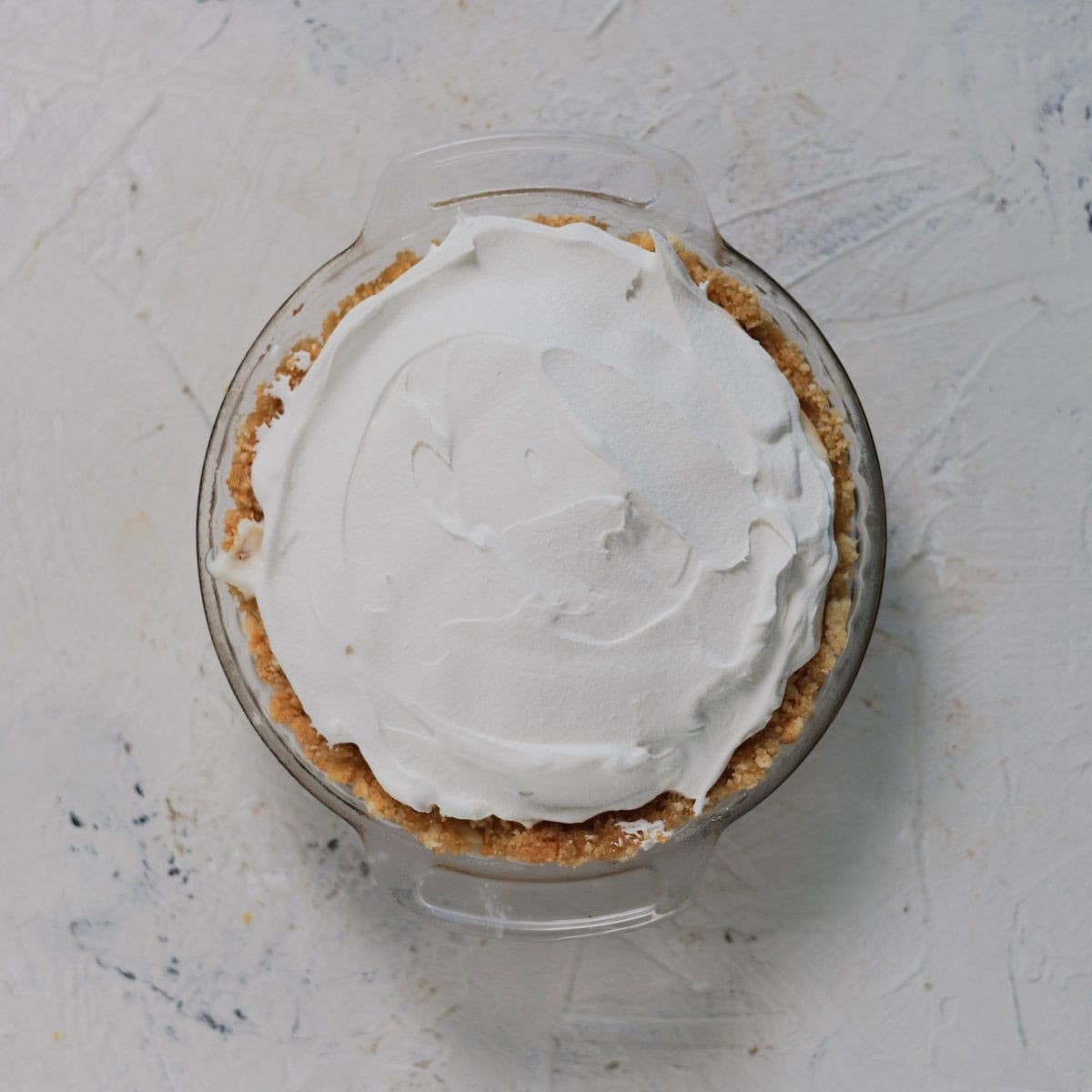 A pie in a glass dish topped with a thick layer of whipped cream.