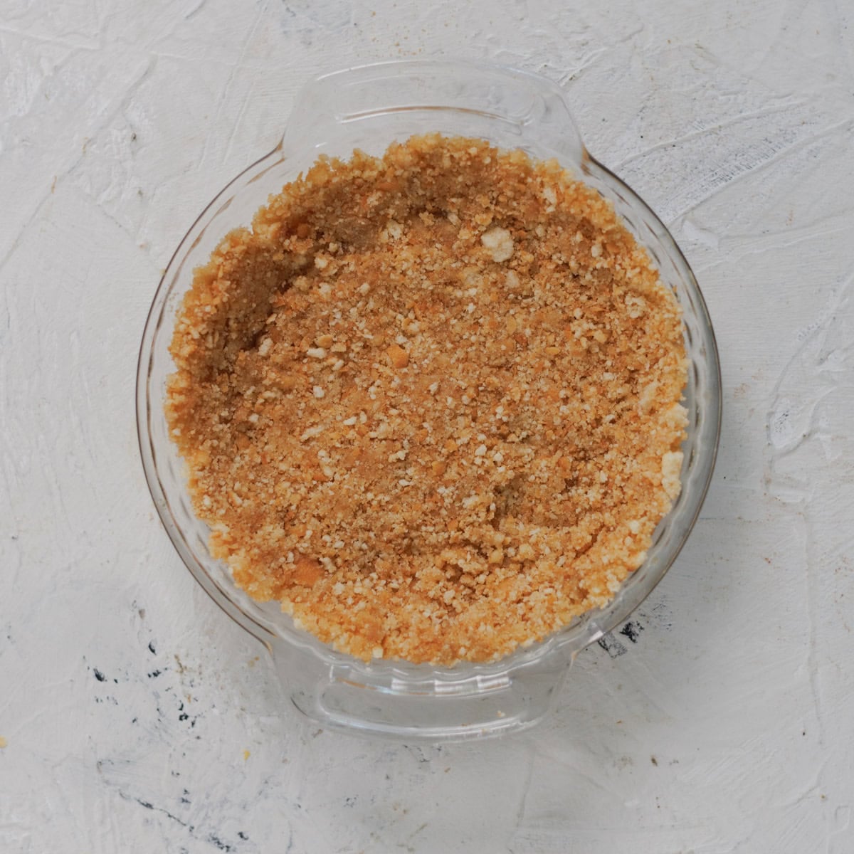 A glass pie dish containing an unbaked crumb crust.