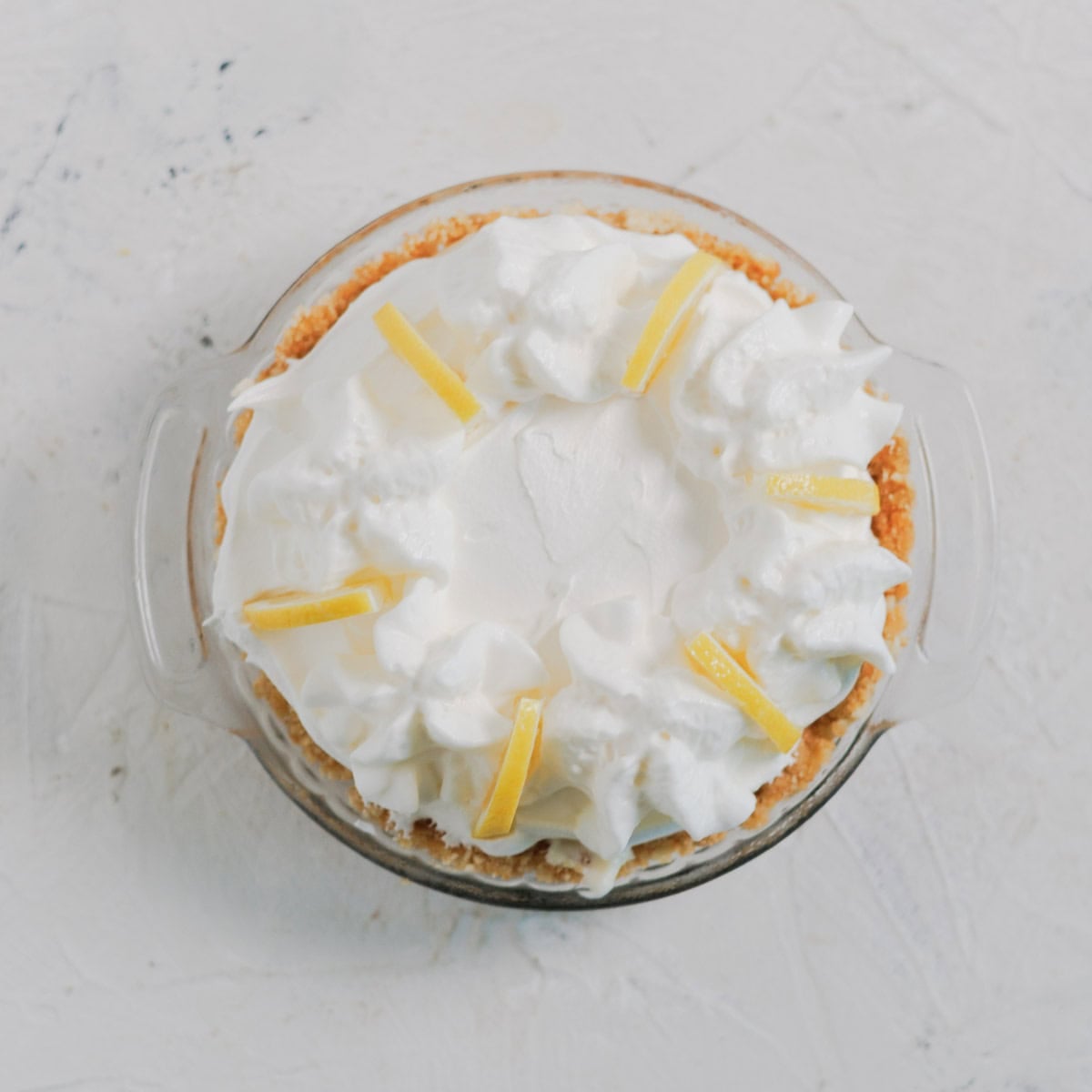A cream pie in a glass pie dish, topped with whipped cream and lemon slices.